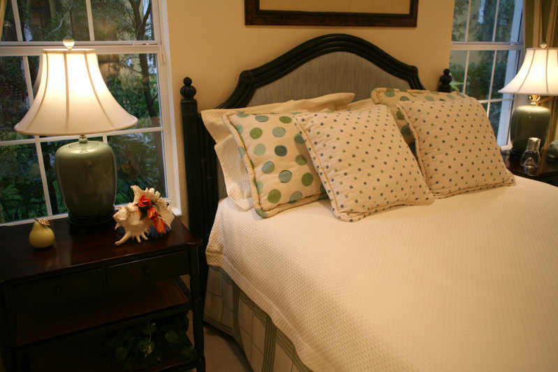 This cheerful bedroom adds a touch of whimsy with green and baby blue polka dotted pillows. The cream linens of the blanketing offer a beautiful canvas that allow these accents to stand out. Larger polka dotted pillows are placed behind more delicately dotted square accent pillows, both of which tie the room together and coordinate with similar color splashes throughout the room.