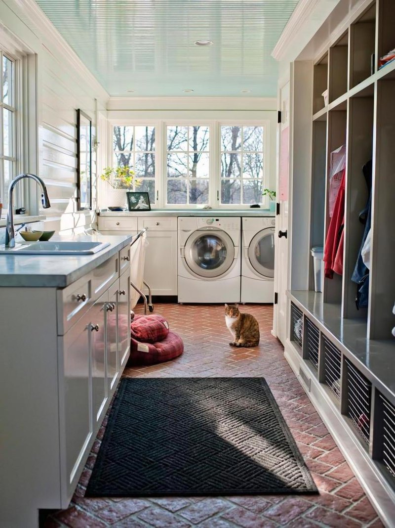 Narrow hallway space in the washing room designed with simply shelving and white sink cabinets by the windows decorated by rug on the brick floor