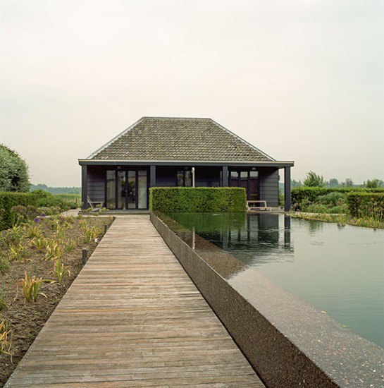 Garden with decking, granite water feature and plants leading to a pool house