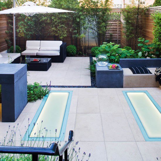 Limestone paved modern garden with black sofas and benches and white parasol