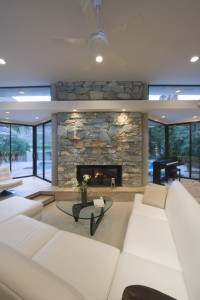 Bright white U-shaped sectional wraps around oblong glass coffee table in front of large stone-wall fireplace in this glass-surrounded living room.