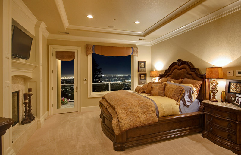 Luxury bedroom with fireplace, TV, balcony access with city views and large wood bedroom furniture.