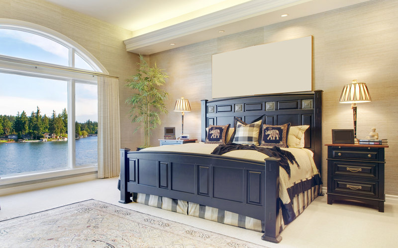 Bright airy master bedroom design with large window overlooking a lake. The star of this bedroom is the king-size bed and matching night stands.