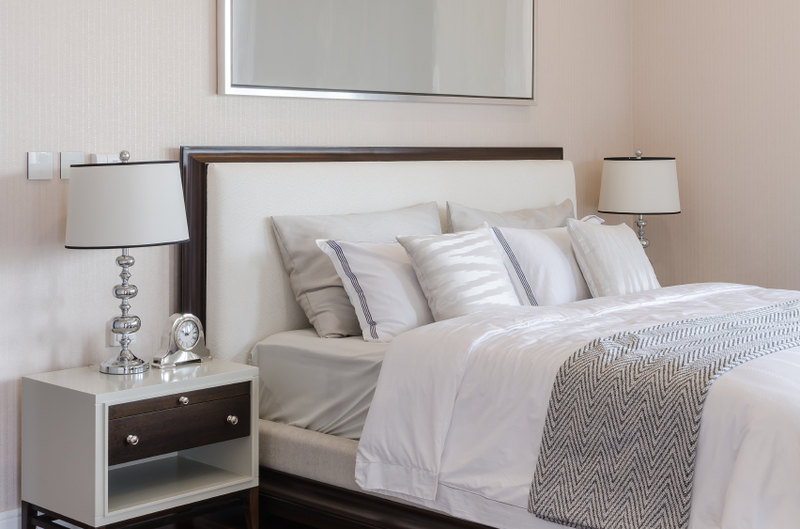 This soft room is crisp and classic. Neutral grays and beige hues offer a restful and attractive sleeping area, while the pillow arrangement features complementary light colors in a pleasing manner. Lightly patterned square accent pillows are placed against white pillows with dark trim for contrast, while large gray sleeping pillows rest against the coordinating padded headboard.