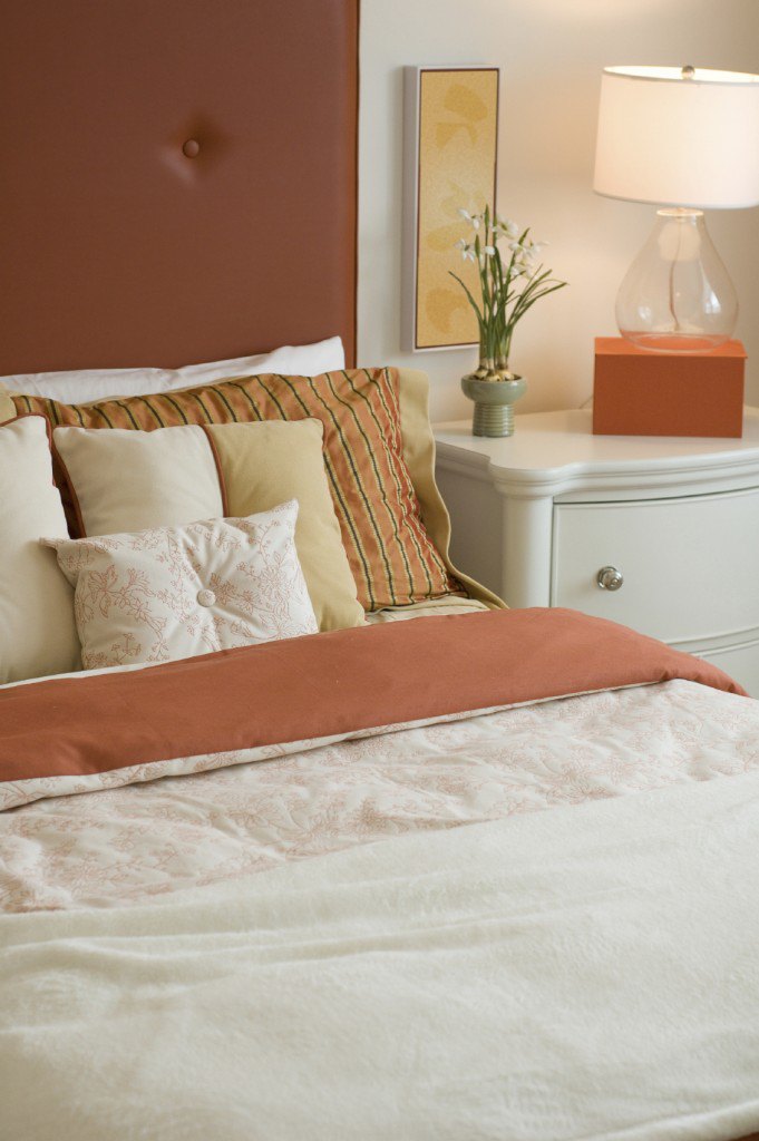 The deep peachy salmon splashes of color throughout this room offer a nice contrast against the blanch backdrop and furnishings. Striped accent pillows host a series of smaller neutral pillows, with a lovely white rectangular patterned piece in front.