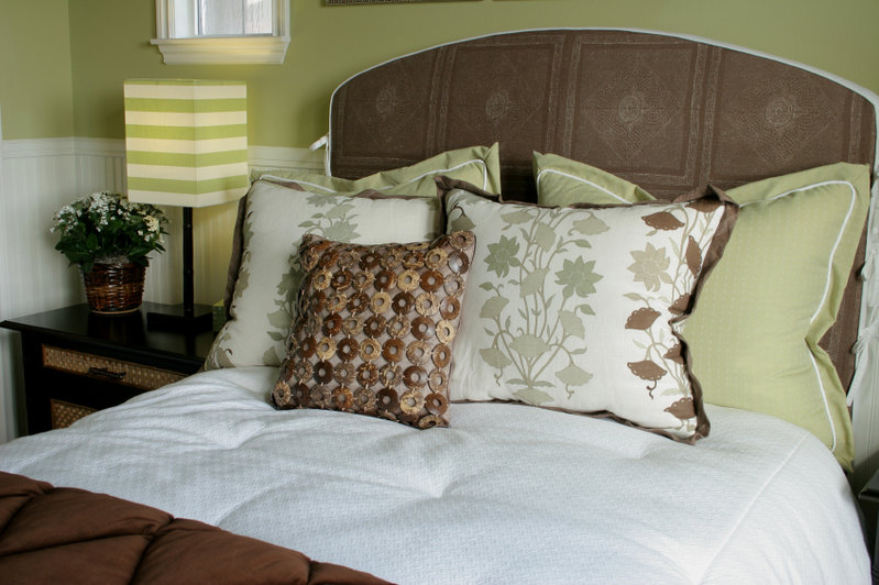 This wonderful arrangement is rich in color and texture. Sage pillows rest against a dark textured headboard, while light and patterned pillows support an unique chain pillow featuring various brown and beige stone or wood links. A striped lampshade coordinates perfectly and adds additional interest, while a lightly textured white comforter promises a soft and relaxing space.