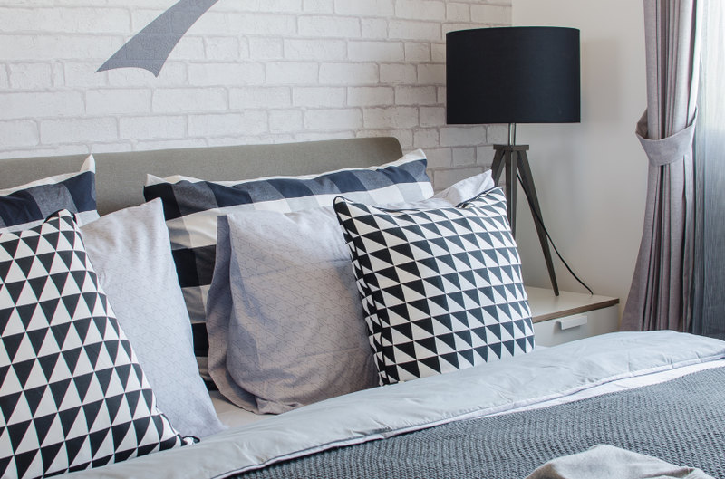 Black and white checked throw pillows stand out against the simple backdrop of the white painted brick wall. Variations in gradient and patterns add interest and appeal to a space that might otherwise be bland.