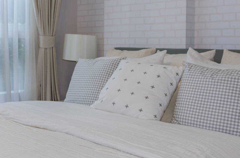 Simple square throw pillows in varying patterns make a big impact against the white brick wall and ivory linens.