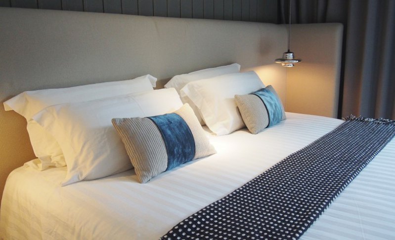 Bold splashes of turquoise are wrapped around rectangular accent pillows, providing necessary interest and contrast to the snow white linens and neutral walls of this understated bedroom.