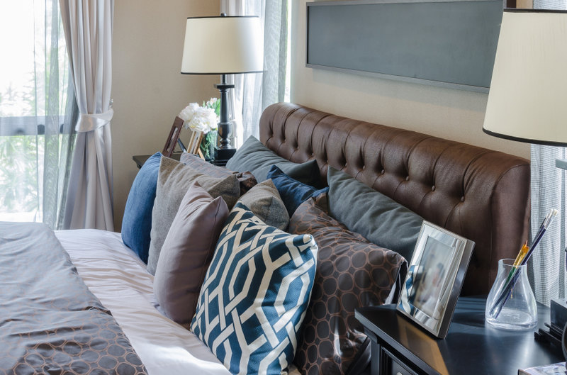 Complementary shades of blues, browns, and grays give this room a comfortable air and a classic feel. A plush leather headboard hosts a plethora of various throw pillows, creating a welcoming and comfortable space that is pleasing to the eye.