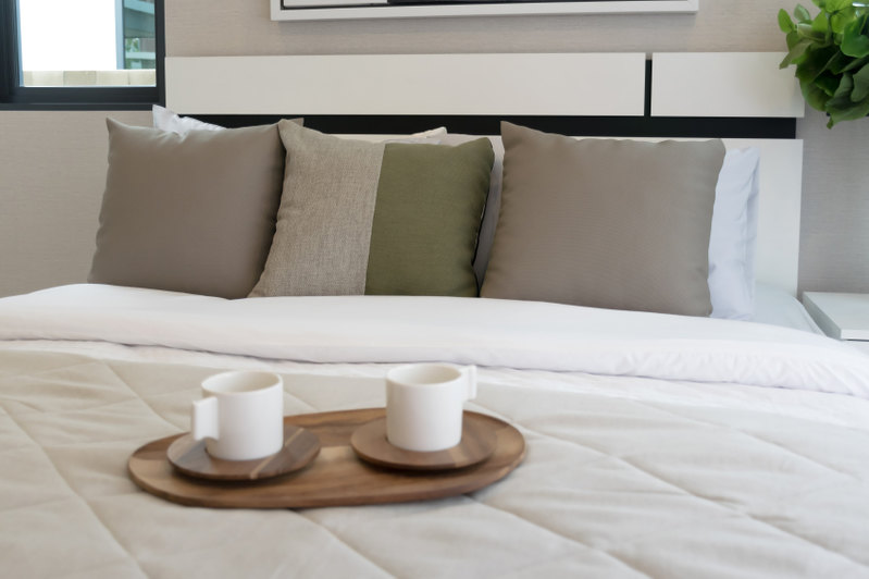Symmetry is employed in a neutral space. Brown throw pillows flank a two toned accent pillow, while the entire lot is supported by traditional white bed pillows.