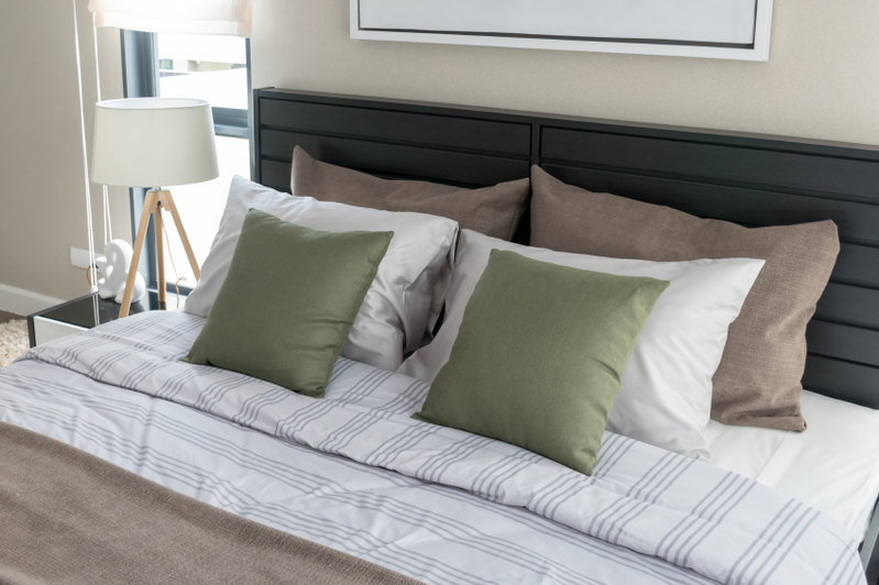 Carefully arranged pillows grace the striped linens of this symmetrical arrangement. The quietly masculine space commands attention without being overwhelming, while a simple headboard oversees the bed offering dark contrast to the neutrals of the room.