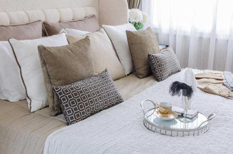 Another impeccable display of the beauty that can be found in symmetry, this fine space features numerous pillows that mirror image each other, providing harmony and balance to the bed. Awash in neutral beiges with a pop of patterned black for contrast, this space is both dynamic and restful.