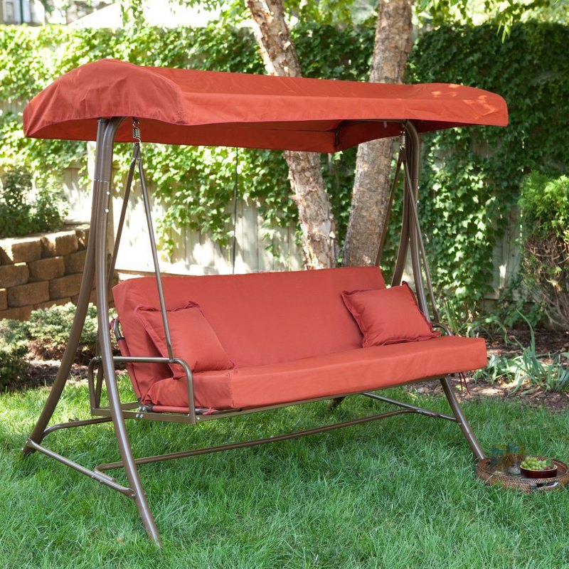 Red Swing Set On Green Grass Near Concrete Fence With Garden