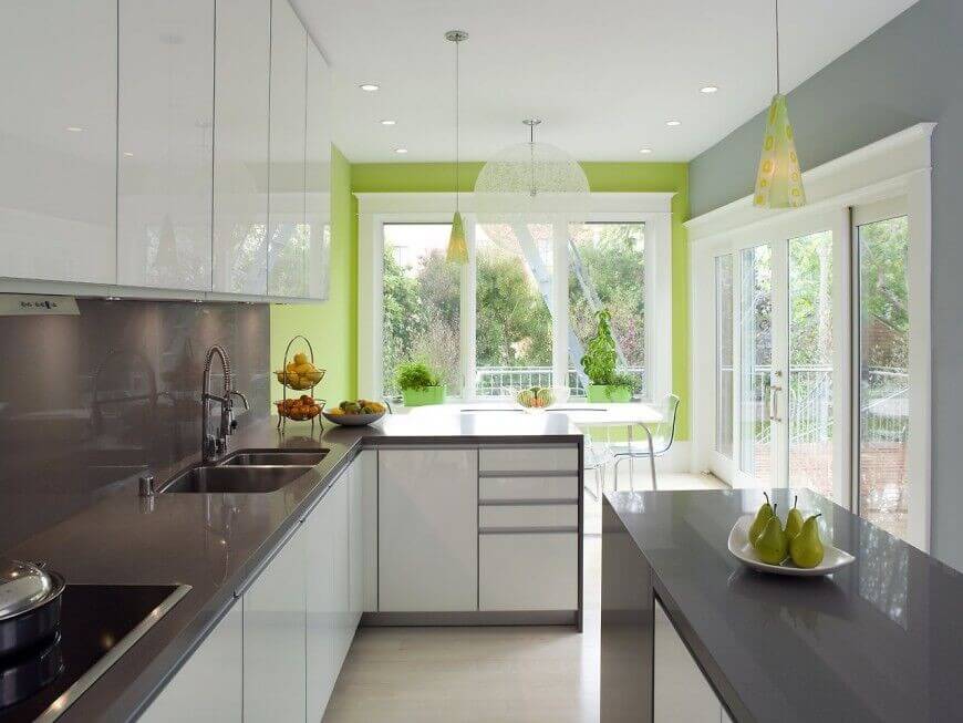 This color scheme of white, grey, and bright green differentiates this kitchen from others of the same contemporary style and keeps the bright white cabinets from overpower the rest of the room. Keeping the high-gloss finish of the cabinets and counters the same throughout the kitchen helps to reflect the light from the large windows further into the room.