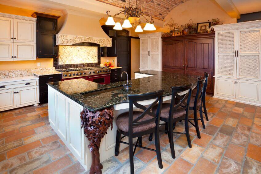 This charming, rustic kitchen successfully combines several different textures and materials to create a cohesive room. The bright shades of the tile floor are reflected in the arched brick ceiling and the golden walls. The granite countertops are complemented by the dark cabinets and tile framing the stove area, as well as the dark wooden chairs standing attention at the island bar.