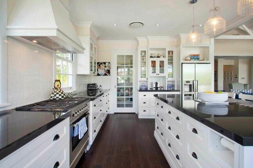 This gorgeous contemporary kitchen utilizes dark granite counter tops and wood flooring to break up the use of bright white. Glass fronts on the upper cabinets and window panes in the pantry door assist this purpose and allow pops of accent colors to show from the inside. The highly reflective surface of the counters keeps them from feeling to heavy in such a light space.