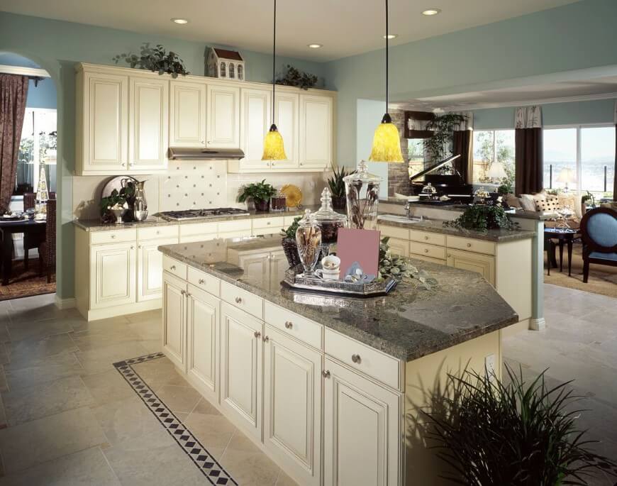 These stunning granite counters go well with the off-white cabinetry and powder blue walls. Accent tiles are pulled up into the room from the floor around the island and into the backsplash behind the stovetop. The kitchen maintains the rich feel of the rest of the house visible in the background.