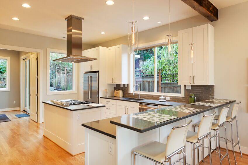 This beautiful, bright kitchen utilizes the white and grey color scheme that is popular in contemporary kitchens. The sleek cabinets complement the clean edges of the appliances and granite countertops. The light grey subway tiles add texture and interest to the space while the light wood floor brings warmth to the room.
