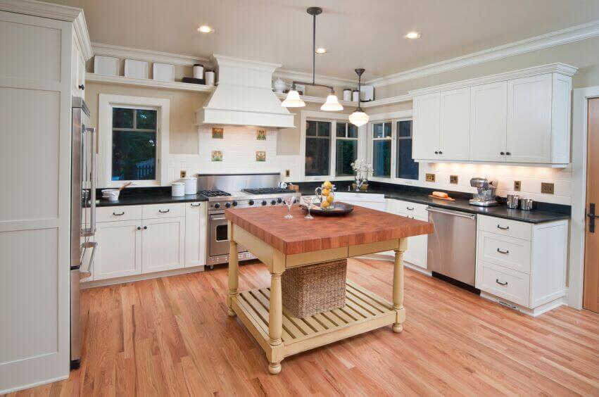 The dark counters in this kitchen break up the white of the cabinets and keep it from being overpowering. The wood of the floor and the island countertop warm up the room while the butter-yellow of the island\\'s base adds a touch of color.