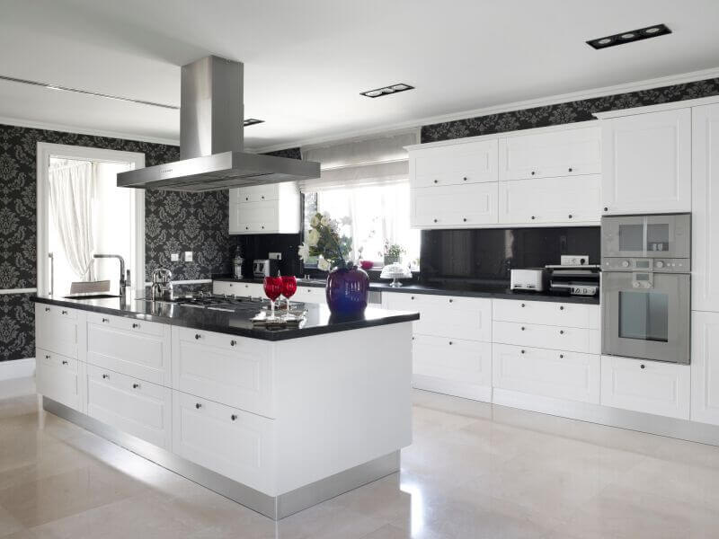 This striking, contemporary kitchen utilizes black counters and bold accent wallpaper to break up the use of white in the room.