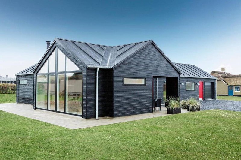 a remarkable side view of black wooden house with glass window and concrete flooring and grassy field