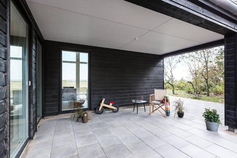 an exciting concrete veranda with classic wooden chair in an enchanting black wooden house with glass window and natural surroundings