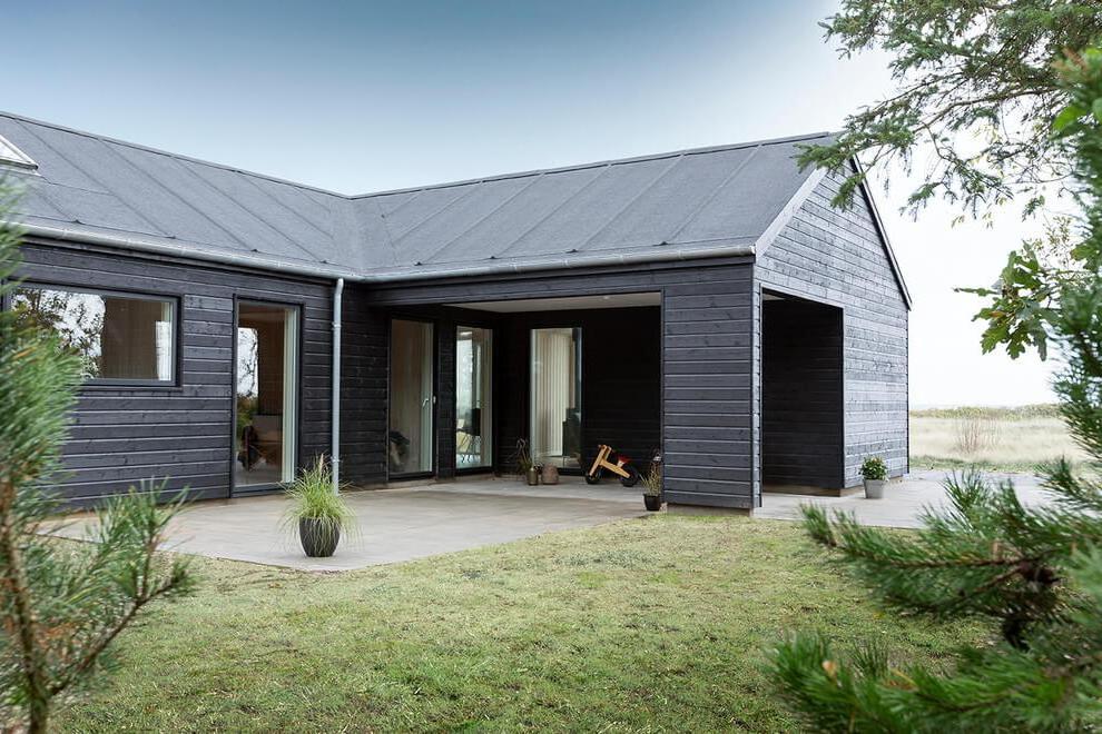 an elegant veranda with concrete flooring in beautiful black wooden house with grassy field