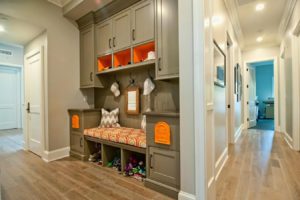 Bright hallway with gray cupboard and shoe storage bench also simply wall hooks and small mirror decorated by recessed ceiling lamps