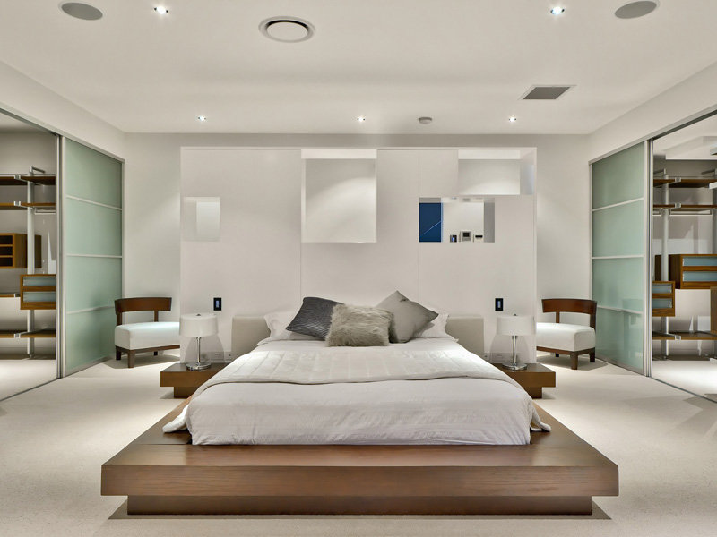 luxurious modern home with white wooden bed and bedside table with a white lamps, white sofa, lighting fixtures with a sliding door.